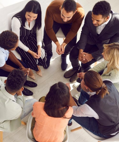 Copy space banner background with coach or psychologist providing professional guidance to group of people. Business team talking while sitting in circle in room with white floor high angle from above